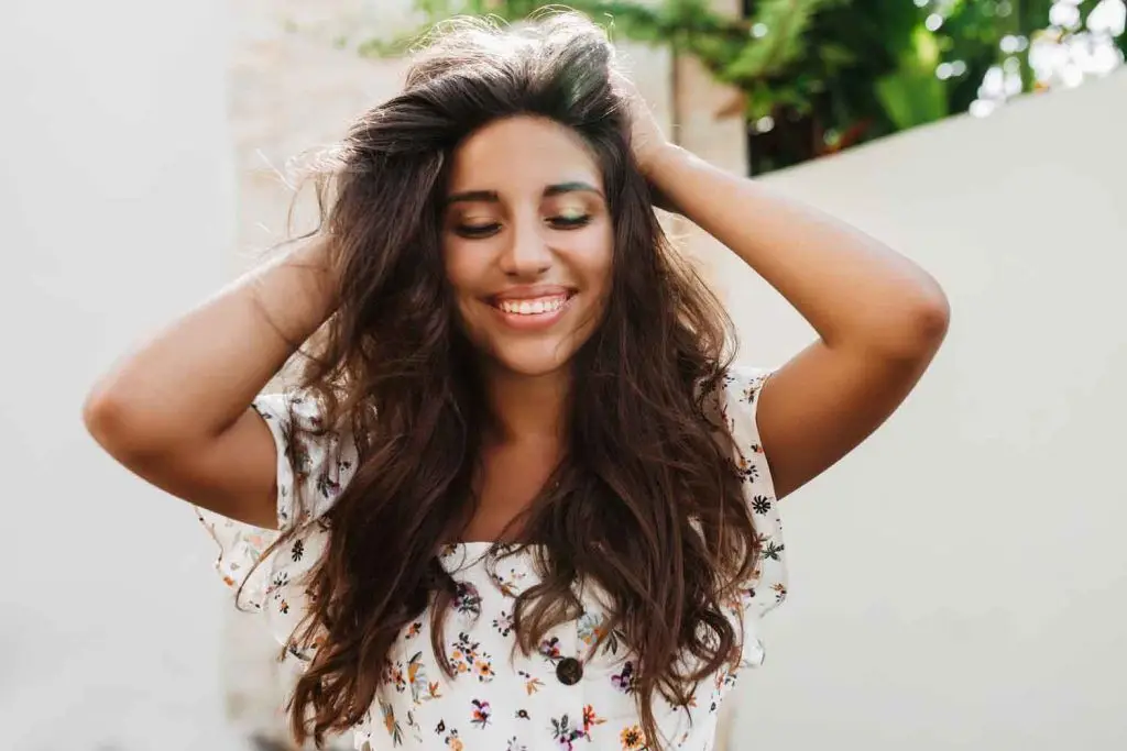 atractiva mujer bronceada blusa blanca con sonrisa encantadora posando pared blanca con plantas verdes